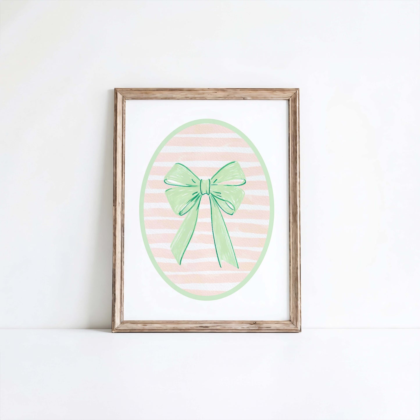 Green bow nursery wall art print with a pink and white striped oval background, shown in a wooden frame. Chic and preppy decor for a baby girl's room.
